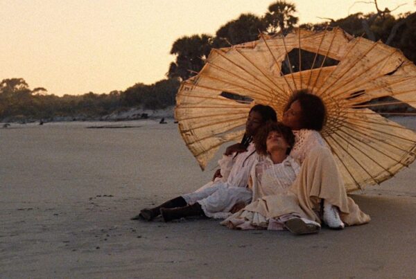 The women sitting together under an umbrella while holes in it on the beach in 'Daughter of the Dust'