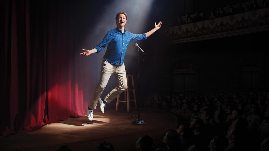 Pete Holmes (Pete Holmes) in a blue shirt floating on a stage in 'Crashing'